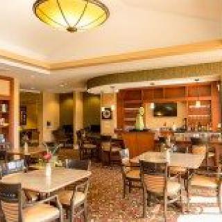 A cozy restaurant interior with neatly arranged tables and chairs, featuring warm lighting and a small bar area.