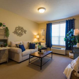 A cozy living room with a comfortable sofa, coffee table, and decorative elements, including indoor plants and stylish curtains.