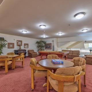 A cozy lounge area with multiple tables and chairs, featuring a carpeted floor and warm lighting.