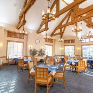 A spacious dining room with wooden beams, elegant chandeliers, and tables set for guests.
