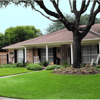 A suburban house with a well-maintained lawn and large tree in the front yard.