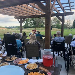 Residents enjoy a lively outdoor performance with snacks in a serene setting.