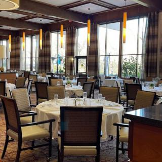 An elegant restaurant dining room with neatly arranged tables and chairs, featuring large windows and stylish lighting.