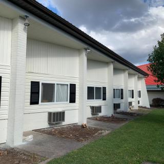 Exterior view of a motel with columns, windows, and a grassy lawn under a cloudy sky.