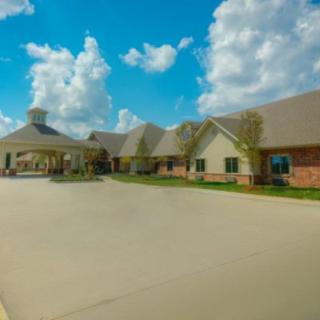 A large building with an entrance driveway under a bright blue sky with clouds.