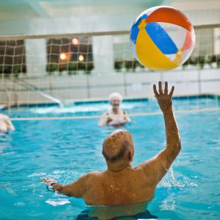 Elderly individuals enjoying a fun game with a beach ball in an indoor swimming pool.