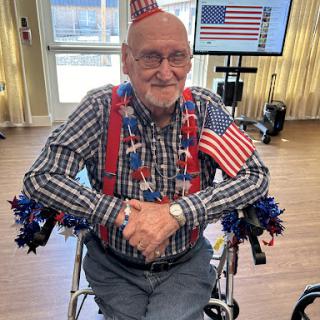 An elderly man dressed in festive patriotic attire, celebrating with American flags and accessories.
