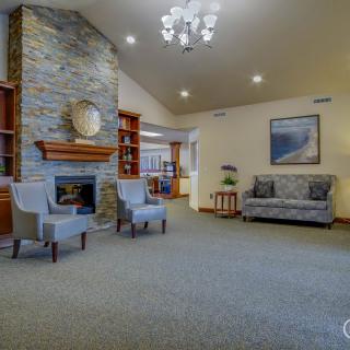 A cozy living room with a stone fireplace, elegant chairs, and a sofa under a chandelier.