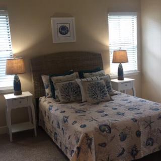 A cozy bedroom with a decorated bed, nightstands, and lamps near two windows.