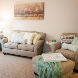 A cozy living room with a beige sofa and armchair, adorned with soft cushions and a decorative painting on the wall.