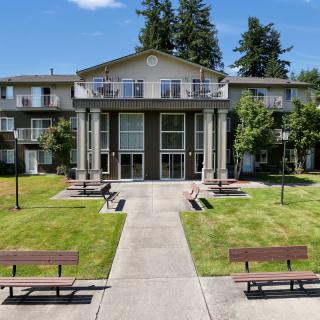 A residential apartment building with a well-maintained lawn and benches in front.