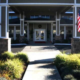 A welcoming entrance to a building with landscaped greenery and an American flag.