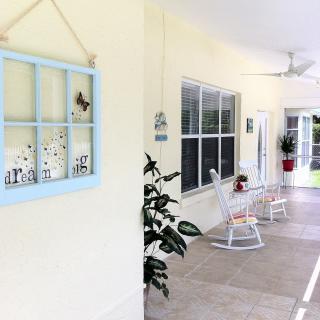 A bright and inviting porch with rocking chairs, wall decor, and large windows.