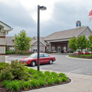 A view of a building with a parking lot and red car under a cloudy sky.