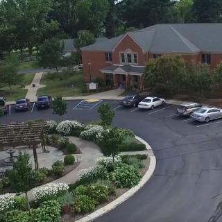 Aerial view of a brick building with a parking lot, surrounded by gardens and trees.