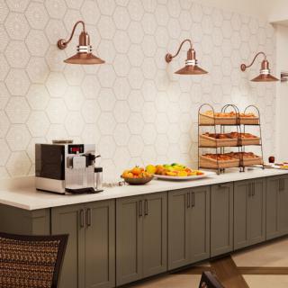 A cozy kitchen setup featuring a coffee machine, fresh fruits, and an assortment of breads on the countertop, illuminated by stylish wall lamps.