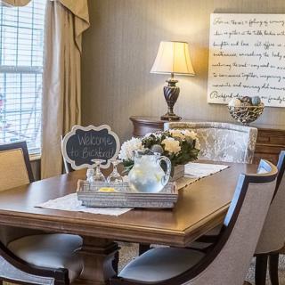 A cozy dining room with elegant decor, featuring a wooden table adorned with flowers and a stylish lamp.