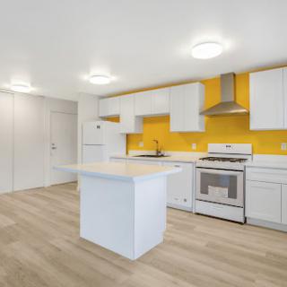 A bright and modern kitchen featuring white cabinetry, a yellow accent wall, and a central island.