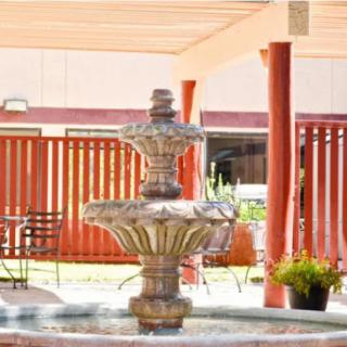 A decorative fountain situated in a sunny outdoor patio area, surrounded by a pergola and garden elements.