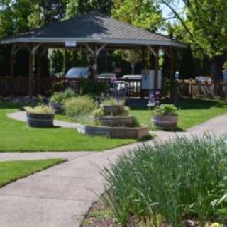 A well-maintained garden featuring a central gazebo, surrounded by lush greenery and intersecting pathways.