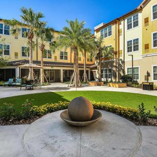 A beautiful courtyard surrounded by a yellow building with palm trees and a central fountain.