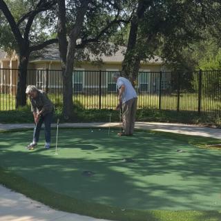 Two men playing on a putting green surrounded by trees.