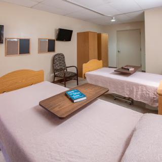 A clean and organized hospital patient room with two beds, a small table, and a television.