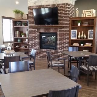 A cozy dining area with a brick fireplace and a television, surrounded by tables and chairs.