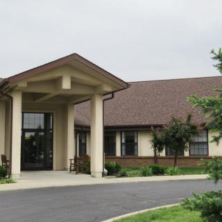 A building with a covered entrance, featuring columns and a well-maintained driveway and surrounding greenery.