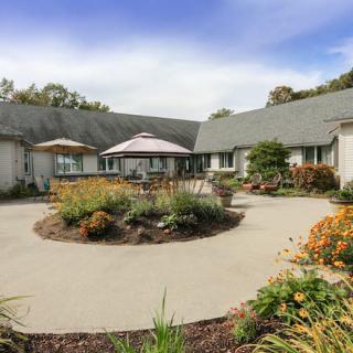 A scenic garden courtyard with vibrant plants and flowers surrounding a patio area at the back of a house.