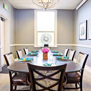 A modern dining room with a large table, surrounded by chairs and adorned with a flower centerpiece.