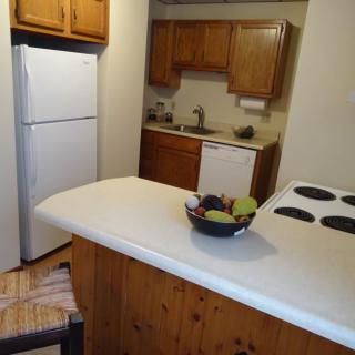 A cozy kitchen with wooden cabinets, a refrigerator, and a countertop with a bowl of fruit.
