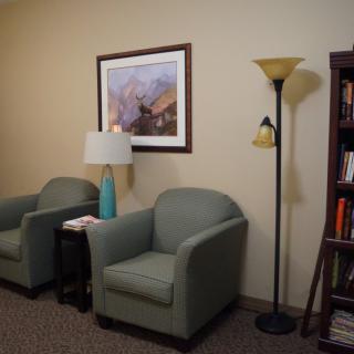 A cozy waiting room with two armchairs, a floor lamp, and a bookshelf.