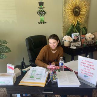 A person sitting at a desk in an office, surrounded by documents and decorations.