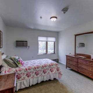 A cozy bedroom with a floral bedspread, a dresser with a mirror, and natural light from the window.