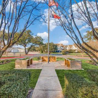 A serene park with a flagpole surrounded by benches and trees under a clear blue sky.