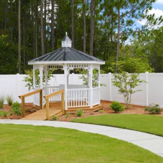 A picturesque gazebo in a well-maintained garden with a white fence and a curving pathway.