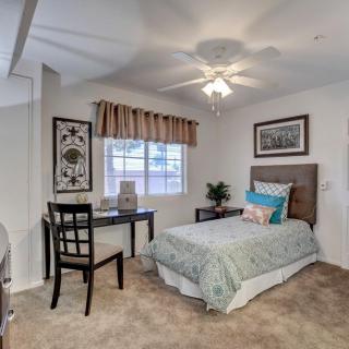 A cozy bedroom with a single bed, desk, and window featuring decorative curtains and artwork on the walls.