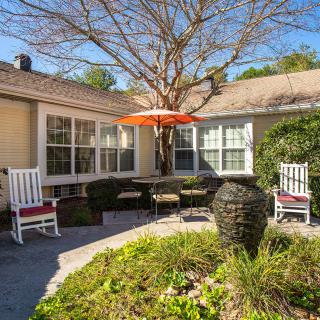 A cozy patio area with rocking chairs and a table under an orange umbrella, surrounded by greenery.