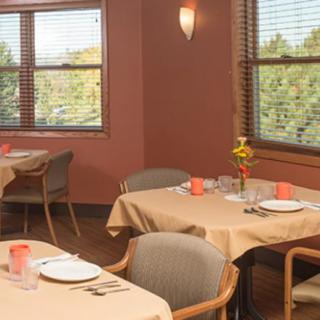 An empty dining room with neatly set tables and chairs, featuring large windows and warm lighting.