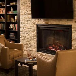 A cozy living room with armchairs by a fireplace and a bookshelf nearby.