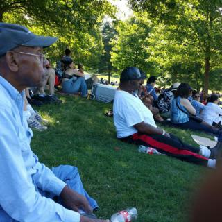 A group of people enjoying a sunny day at the park, sitting on the grass under the shade of trees.