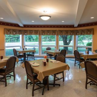 A cozy dining area featuring tables arranged for guests, with large windows allowing natural light to fill the space.