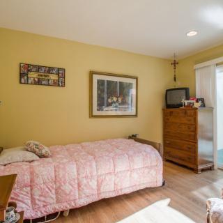 A cozy bedroom featuring a single bed with a pink quilt, a wooden dresser with a television on top, and framed artwork adorns the walls.