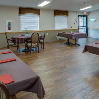 An empty dining room with neatly arranged tables and chairs, featuring wooden flooring and natural light from windows.
