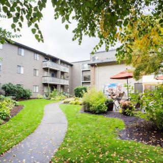 A well-maintained apartment complex with a lush green courtyard and outdoor seating.