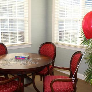 A cozy dining area with a round table, red cushioned chairs, and a red balloon tied to a plant by the window.