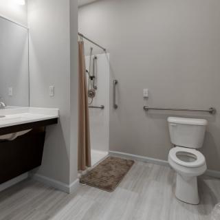 A modern bathroom featuring a toilet, shower, and sink with a mirror.