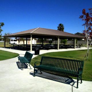 A sunny day at a park with a pavilion and benches along the walkway.