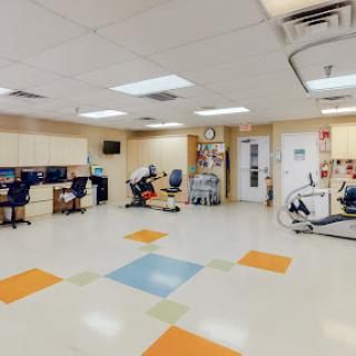 A spacious rehabilitation room equipped with various exercise machines and workstations for therapy activities.